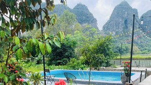 A pool area with a view of mountains, surrounded by lush greenery and red flowers. - Tràng An Sunny River Homestay (Ninh Binh)