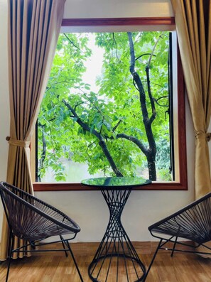 A room with a window overlooking a tree, two black wireframe chairs, and a small glass table. - Tràng An Sunny River Homestay (Hoa Lu)