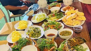 A table with various dishes, including grilled fish, vegetables, and bread, along with several cans of beer. - Tràng An Sunny River Homestay (Hoa Lu)