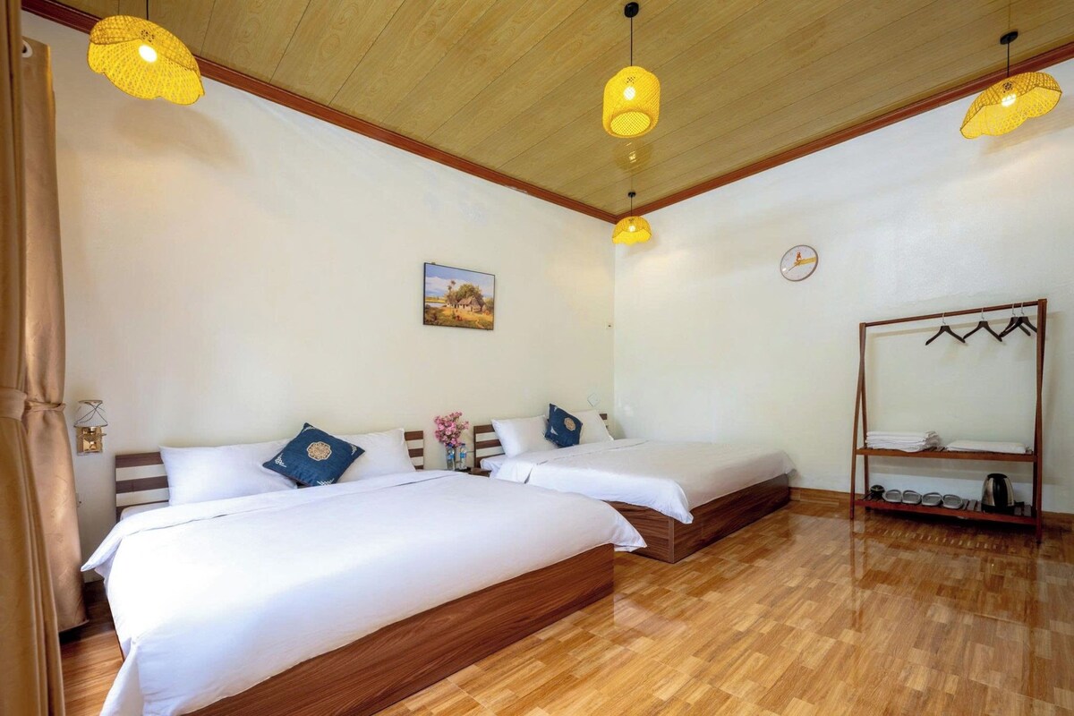A hotel room with two beds, wooden flooring, and hanging lamps.