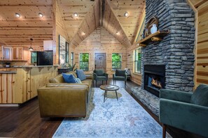Cozy living area with a comfortable sofa, stone fireplace, and large windows offering views of the surrounding greenery.