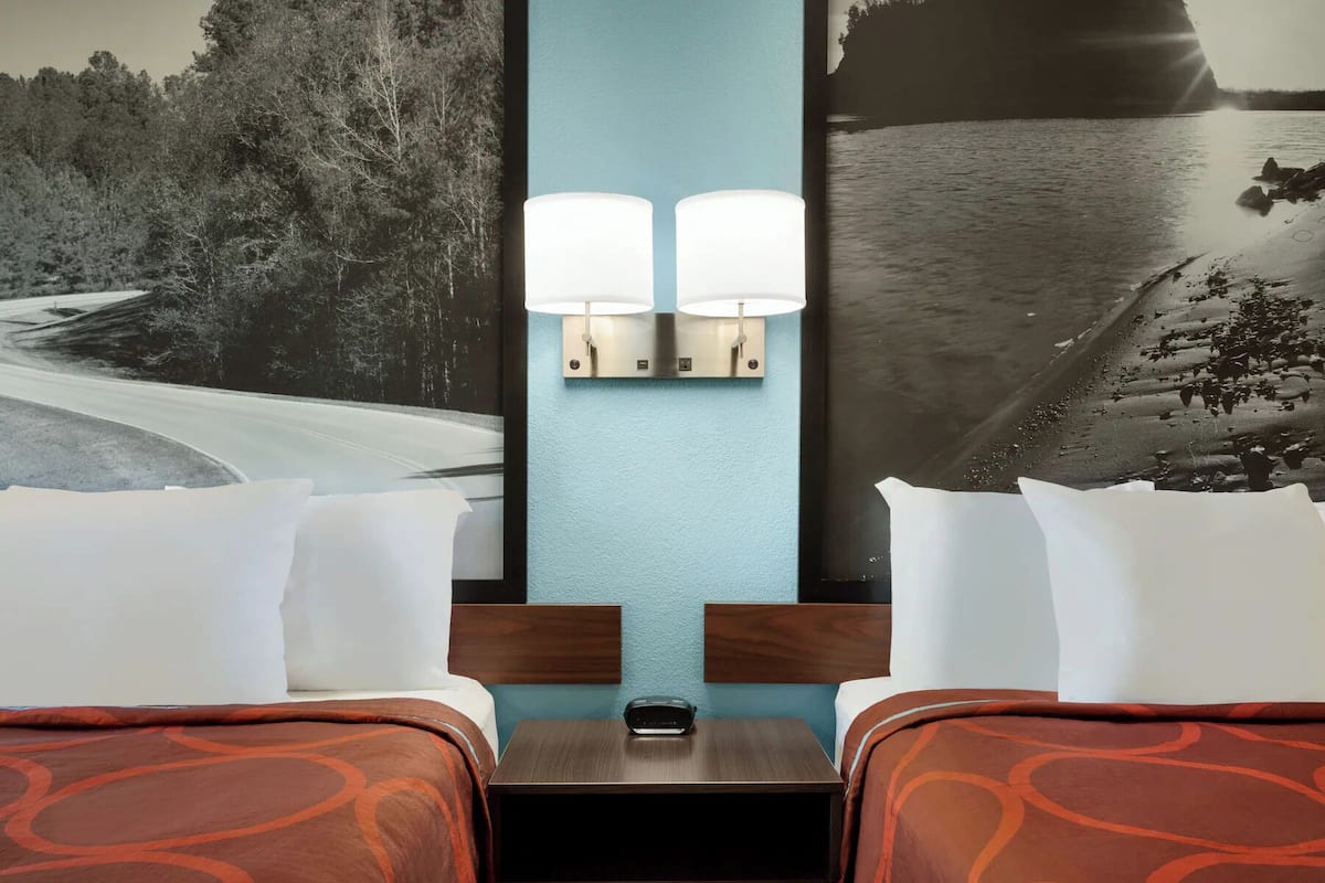 Una habitación de hotel con dos camas, una mesita de noche y una lámpara fijada a la pared.