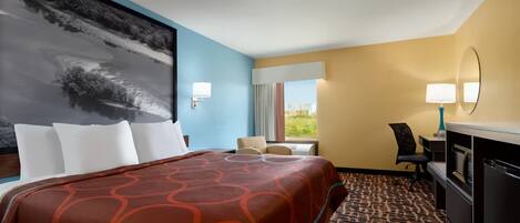 A hotel room with a large bed, a desk with a computer, a chair, and a view of the outdoors through a window.