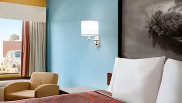 A hotel room with a bed, a chair, a wall-mounted lamp, and a large painting.