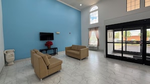 A spacious lobby with a blue wall, two beige sofas, a flat-screen TV, a decorative vase, and a large window with curtains. - Hometown Place Olive Branch (Olive Branch)