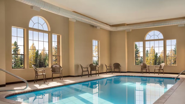 An indoor swimming pool with clear views of trees through large arched windows. - Hometown Place Olive Branch (Olive Branch)