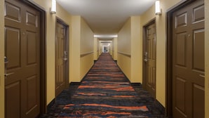 A hotel hallway with carpeted floors, doors on both sides, and light fixtures on the walls. - Hometown Place Olive Branch (Olive Branch)