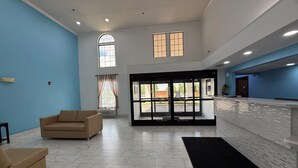 A spacious lobby with a reception desk, a beige sofa, and a large window with curtains. - Hometown Place Olive Branch (Olive Branch)