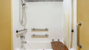 Un baño moderno con bañera, ducha, barras de apoyo y un estante de madera.