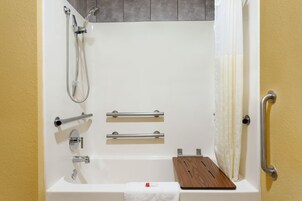 Un baño moderno con bañera, ducha, barras de apoyo y un estante de madera.