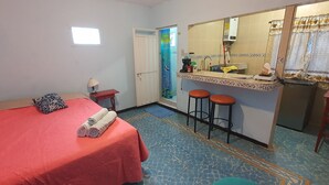 Habitación de hotel con cama, una mesita con lámpara, baño con lavamanos y espejo, y dos taburetes.