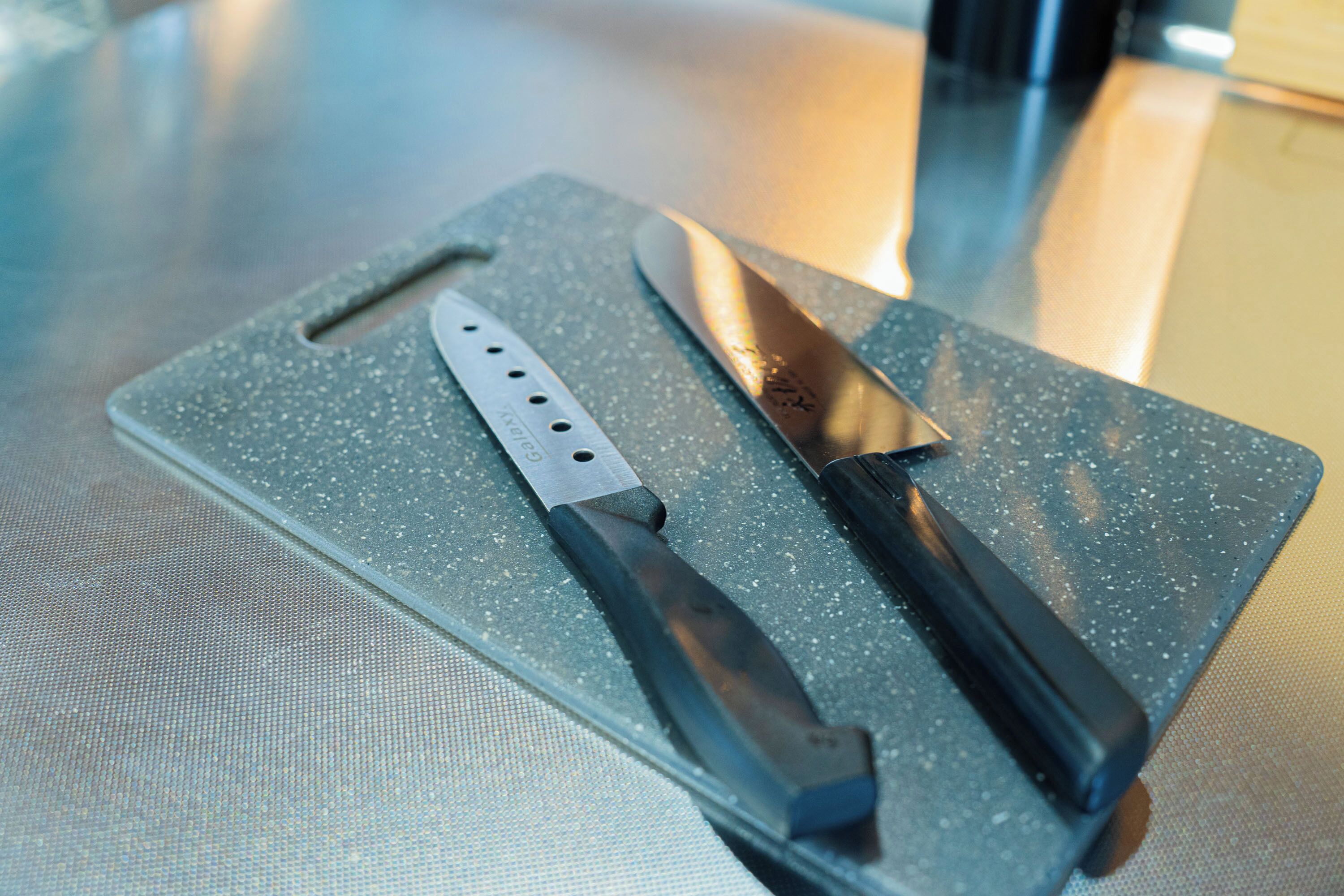 A kitchen counter with two knives and a cutting board.