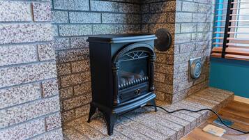 A black wood-burning stove in a corner with a stone wall and a window with blinds.