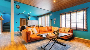 Un salon moderne avec un mur d’accent bleu, un plafond en bois et une grande fenêtre équipée de stores.