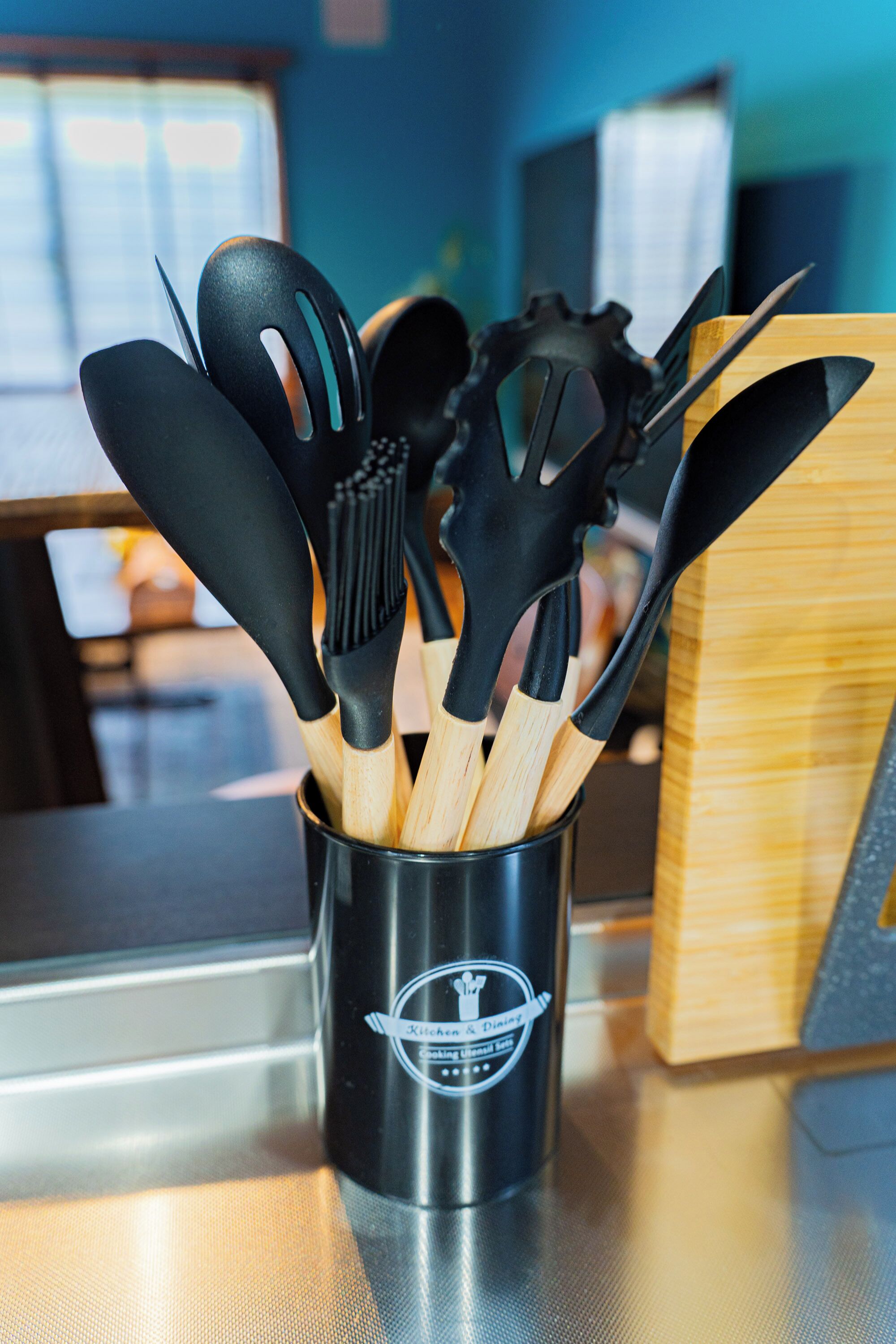 A utensil holder with black and wooden utensils on a kitchen counter.