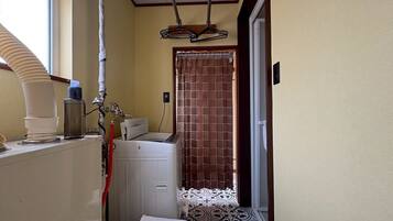 A compact bathroom with a washing machine, a drying rack, and a shower curtain.