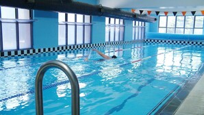 Una piscina interior con marcas divisorias claras, una escalera de metal y ventanas a lo largo de un lateral.