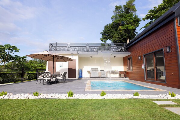 A modern outdoor pool area with a dining set and a covered seating area.