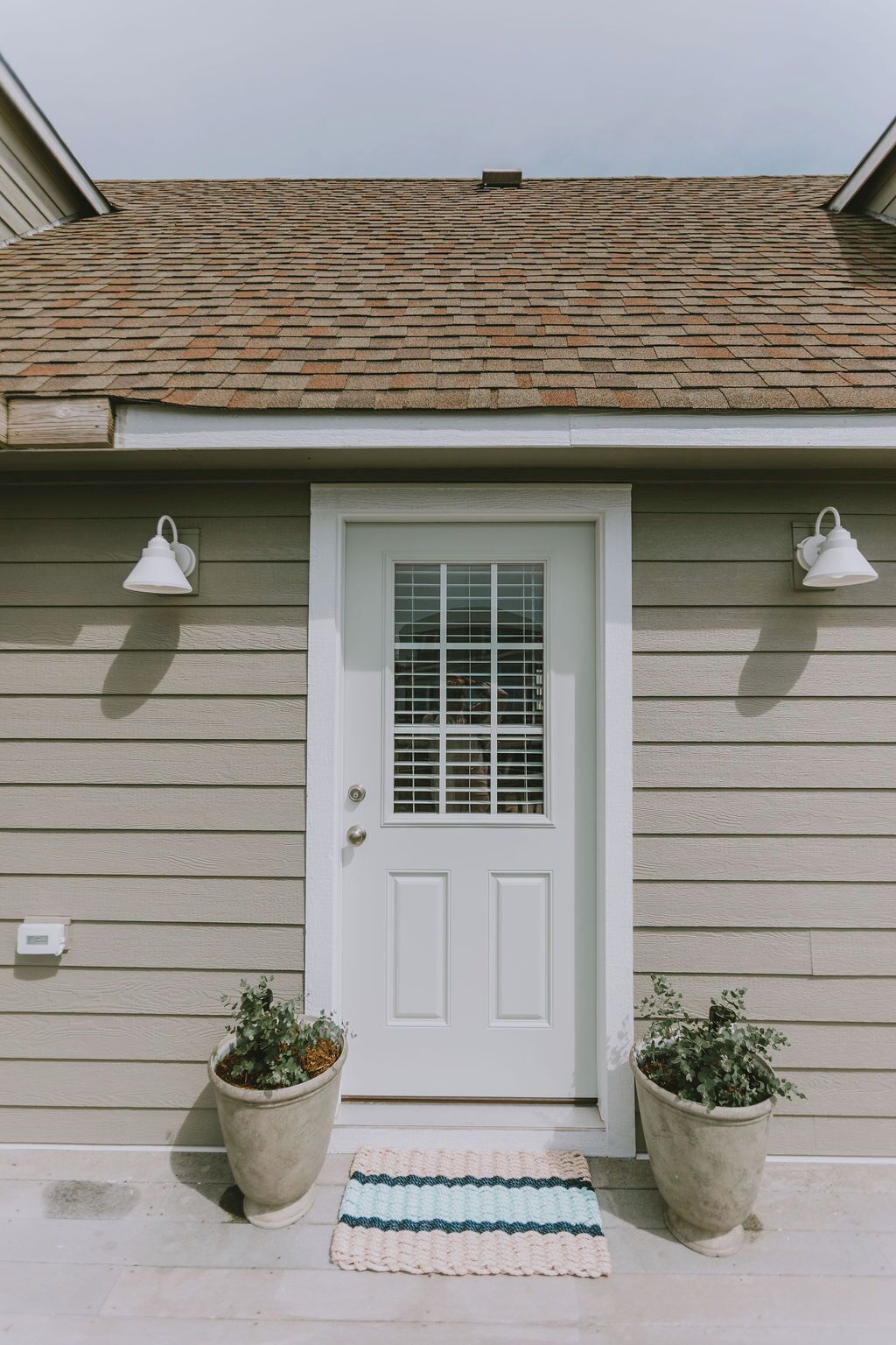A house with a white door, two potted plants, and a striped rug.