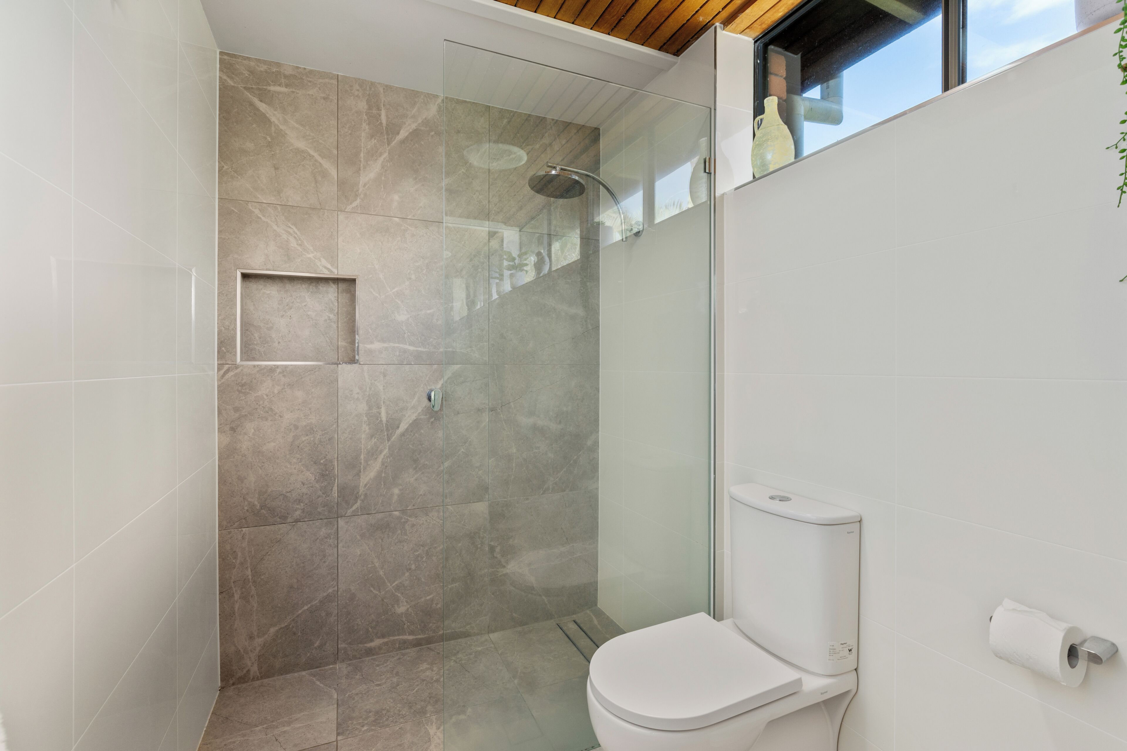 Un baño moderno con cabina de ducha de vidrio, inodoro y ventana sobre el lavabo.