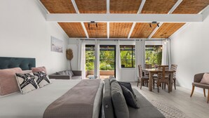 Une chambre dotée d’un grand lit, d’un canapé, d’une table à manger avec des chaises et d’un balcon offrant une vue sur la verdure.