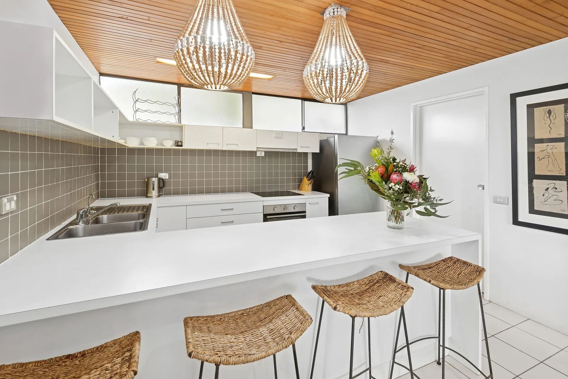 A modern kitchen with a white countertop, stainless steel appliances, and a wooden ceiling.