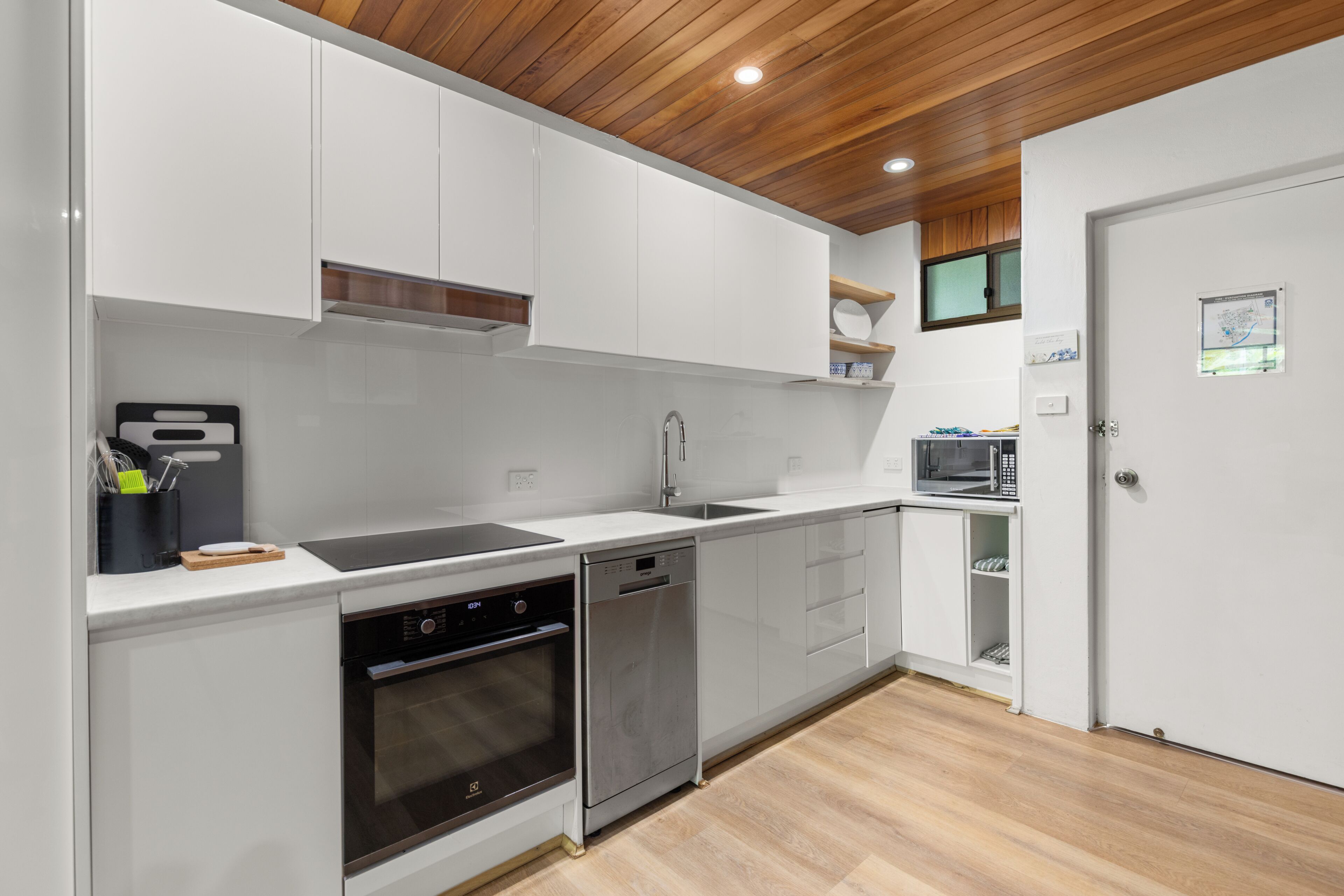 A modern kitchen with white cabinets, a dishwasher, an oven, and a microwave.
