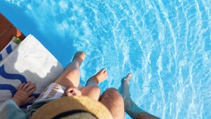 Une piscine avec une eau d’un bleu limpide, une serviette et les jambes d’une personne.