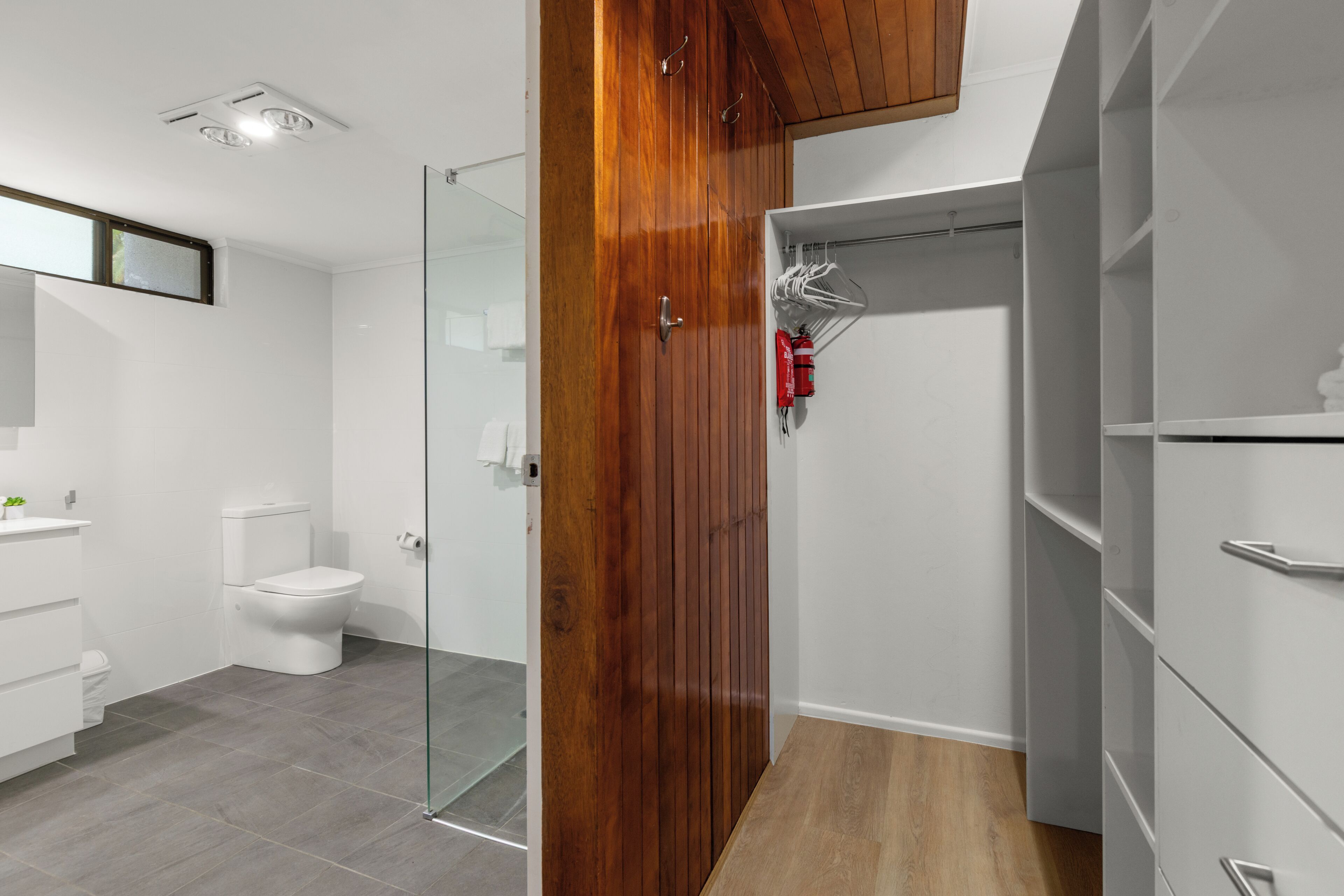 Een moderne badkamer met een glazen douchecabine, een wit toilet en een houten garderobe.
