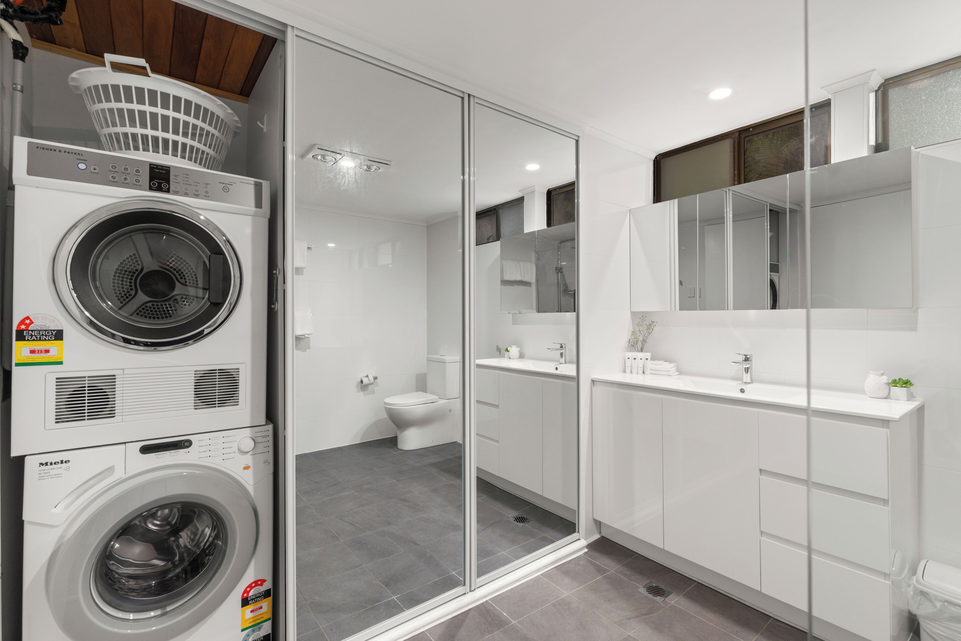A modern bathroom with a glass shower enclosure, a white sink, and a washing machine.