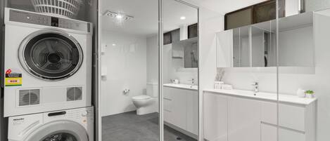 A modern bathroom with a glass shower enclosure, a white sink, and a washing machine.