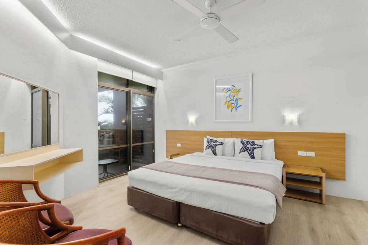 Ein modernes Hotelzimmer mit einem großen Bett, einem Schreibtisch, einem Sessel, einem Deckenventilator und einem Fenster.