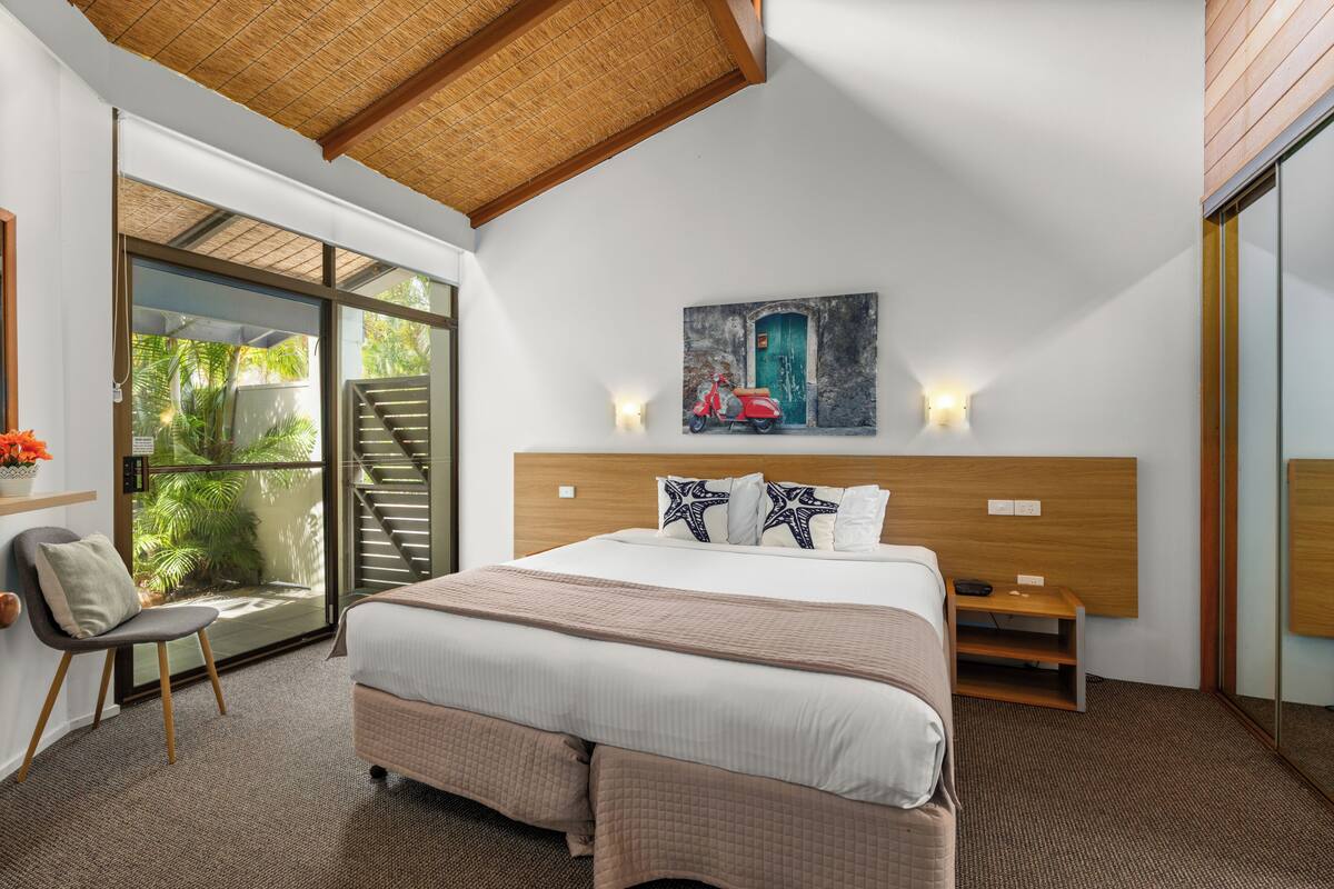 Ein Schlafzimmer mit einem großen Bett, einem Bild von einem Roller, einer TV-Kommode und einer Schiebeglastür zum Balkon.
