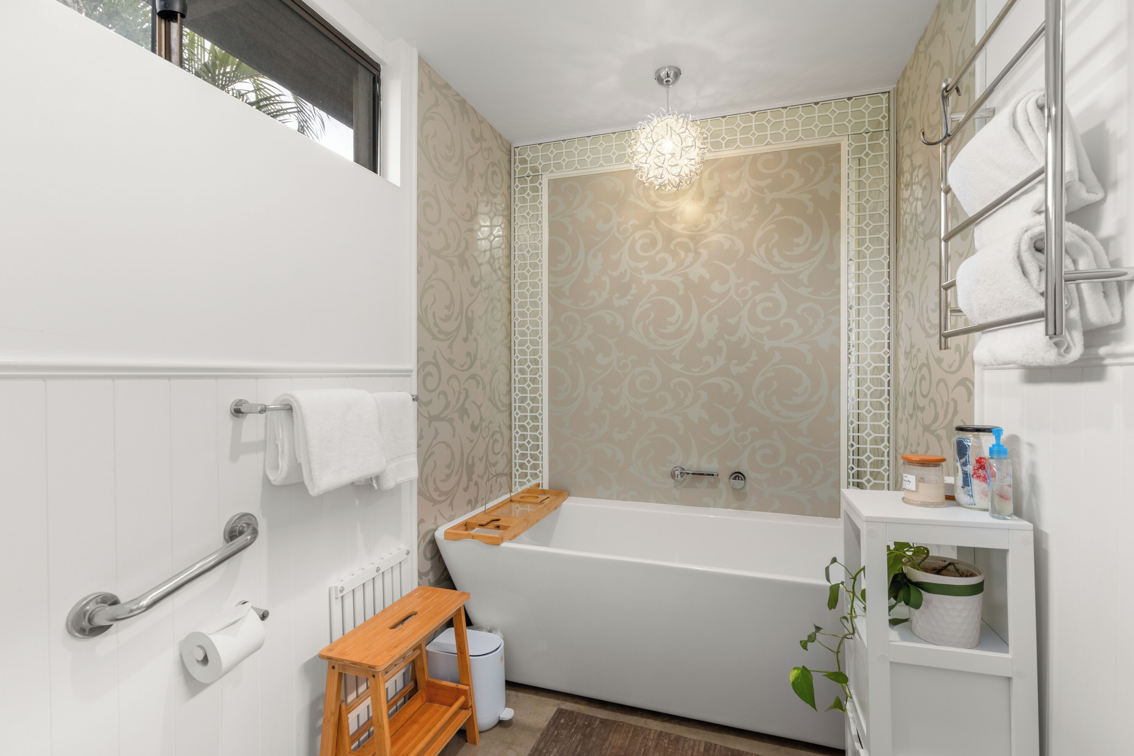 A modern bathroom with a bathtub, a handrail, a toilet paper holder, and a small shelf with toiletries.