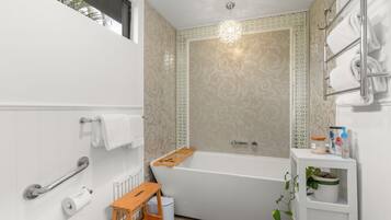 A modern bathroom with a bathtub, a handrail, a toilet paper holder, and a small shelf with toiletries.