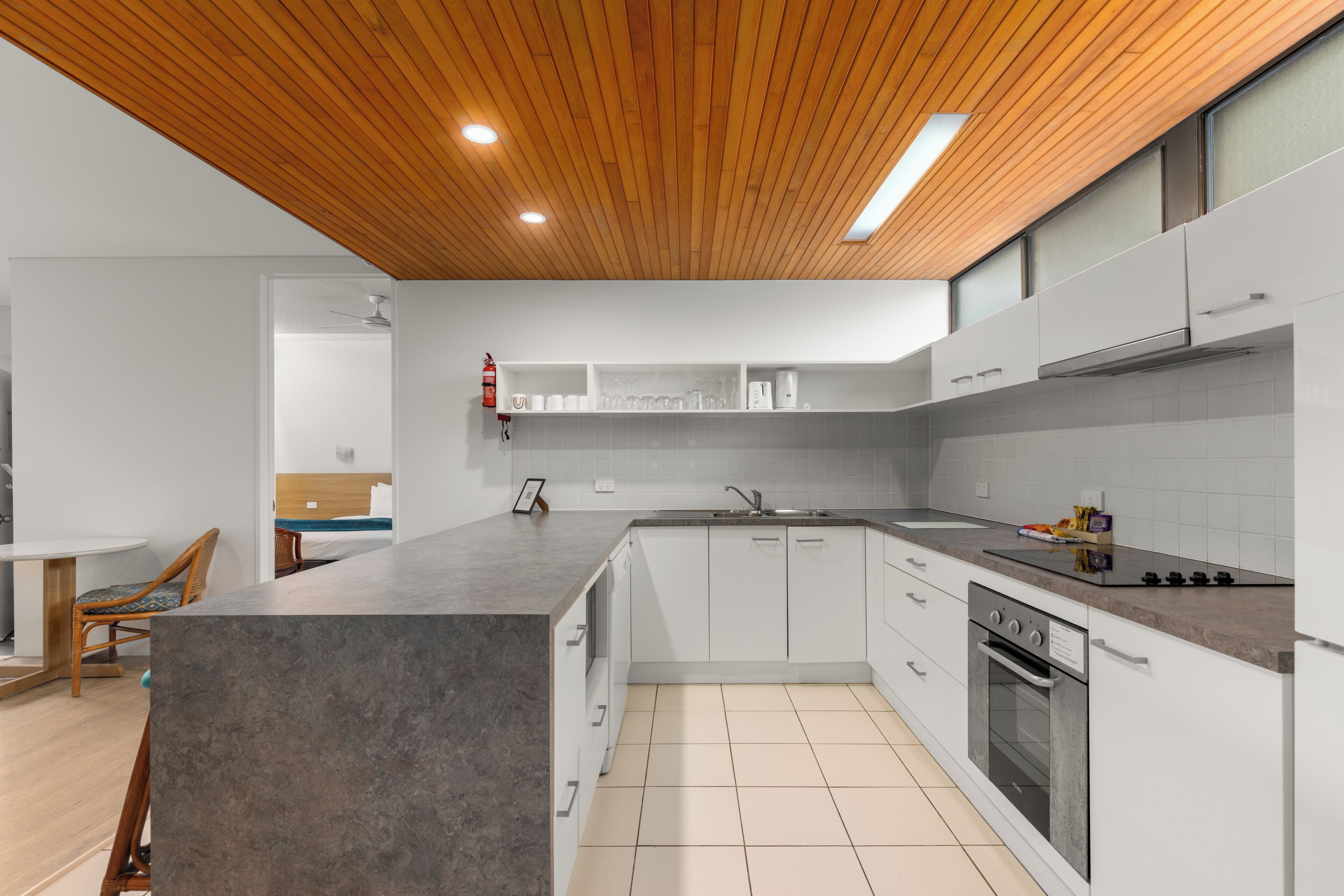 A modern kitchen with a wooden ceiling, white cabinets, a large island, and a built-in oven.