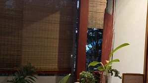 A cozy indoor seating area with wooden furniture, potted plants, and a bamboo blind covering a window. - Rara Guest House Raja Ampat (Waisai)
