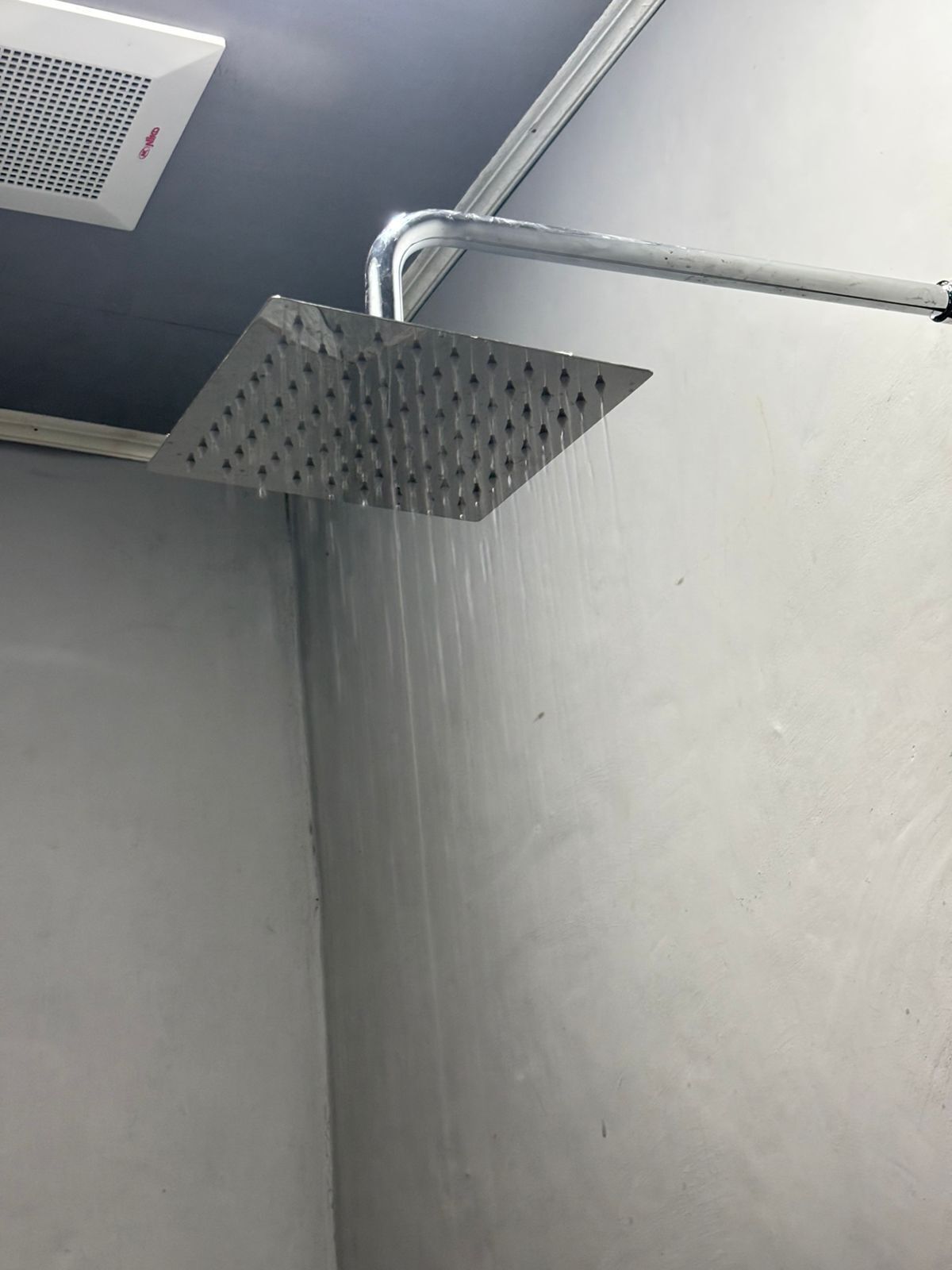 A showerhead with water running, a metal pipe, and a white ceiling vent.
