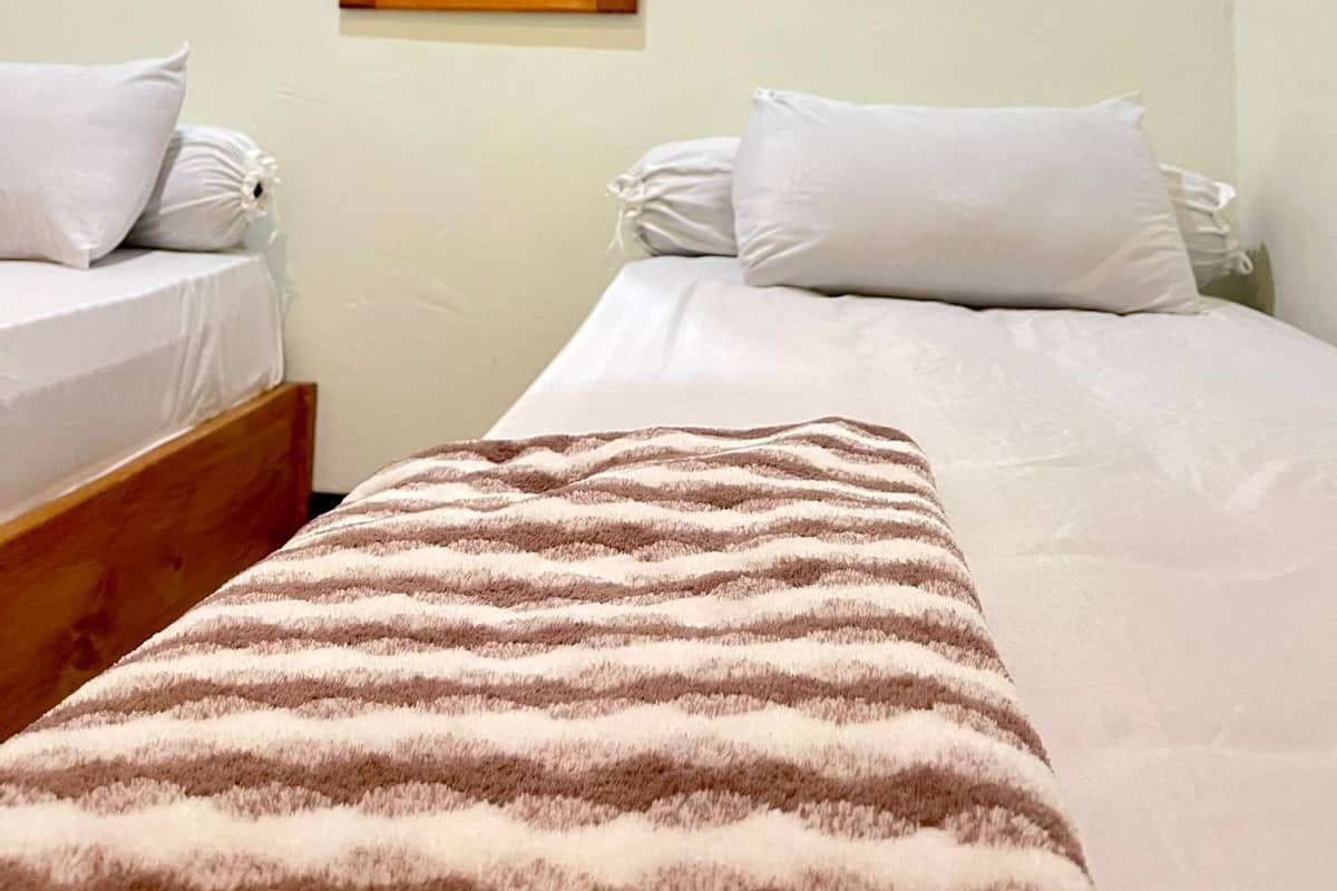 A hotel room with two single beds, a large mirror, and three framed pictures on the wall.