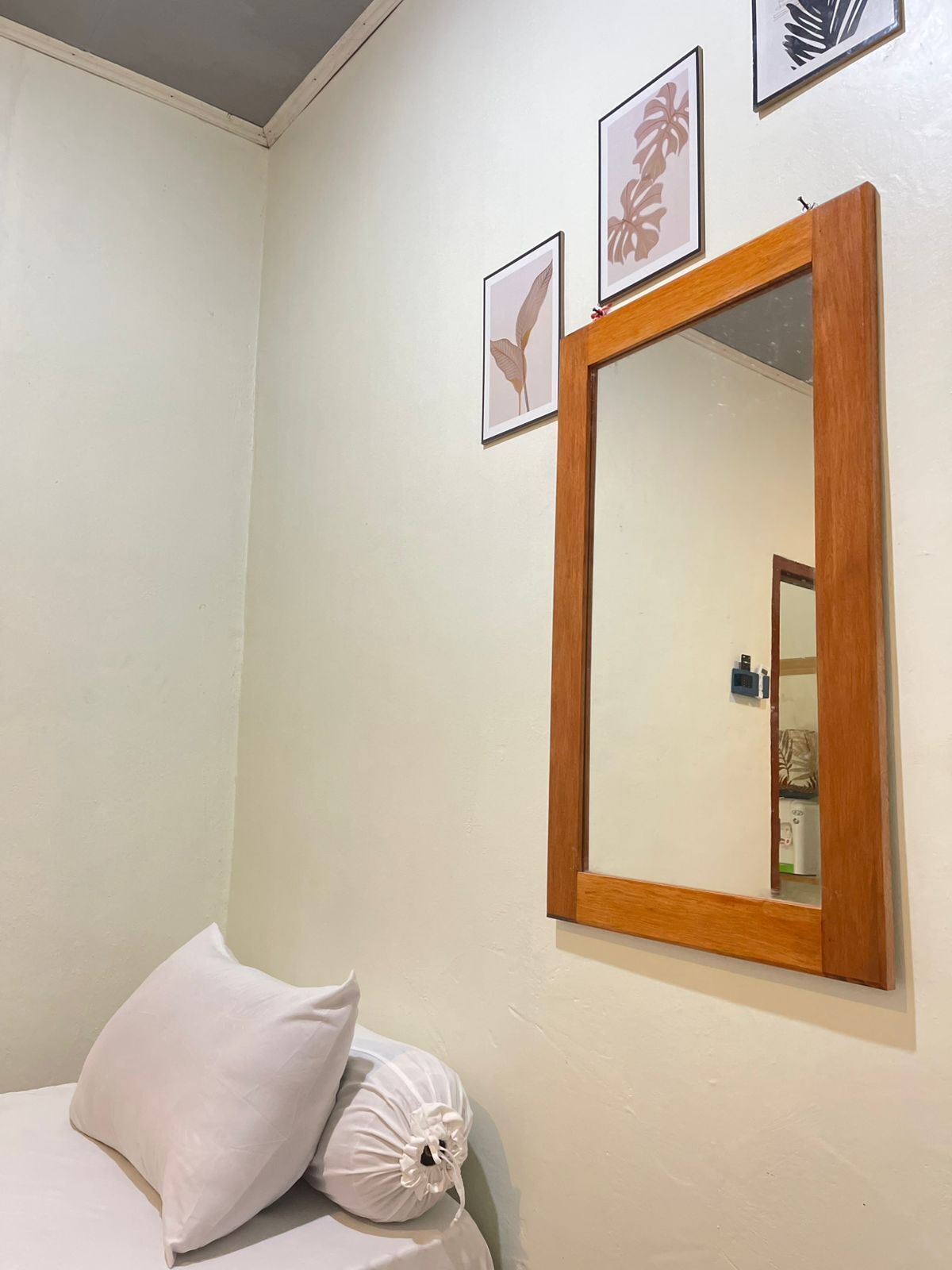 A bedroom with a bed, a wooden-framed mirror, and framed artwork on the wall.