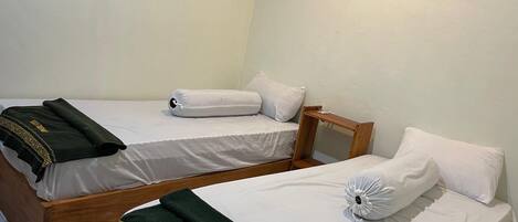 Deux lits simples avec du linge de lit blanc, une table de chevet en bois et une serviette verte avec l’inscription « KIA GUEST HOUSE ».