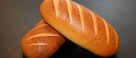 Two loaves of bread with a crusty texture and diagonal slashes on a dark surface.
