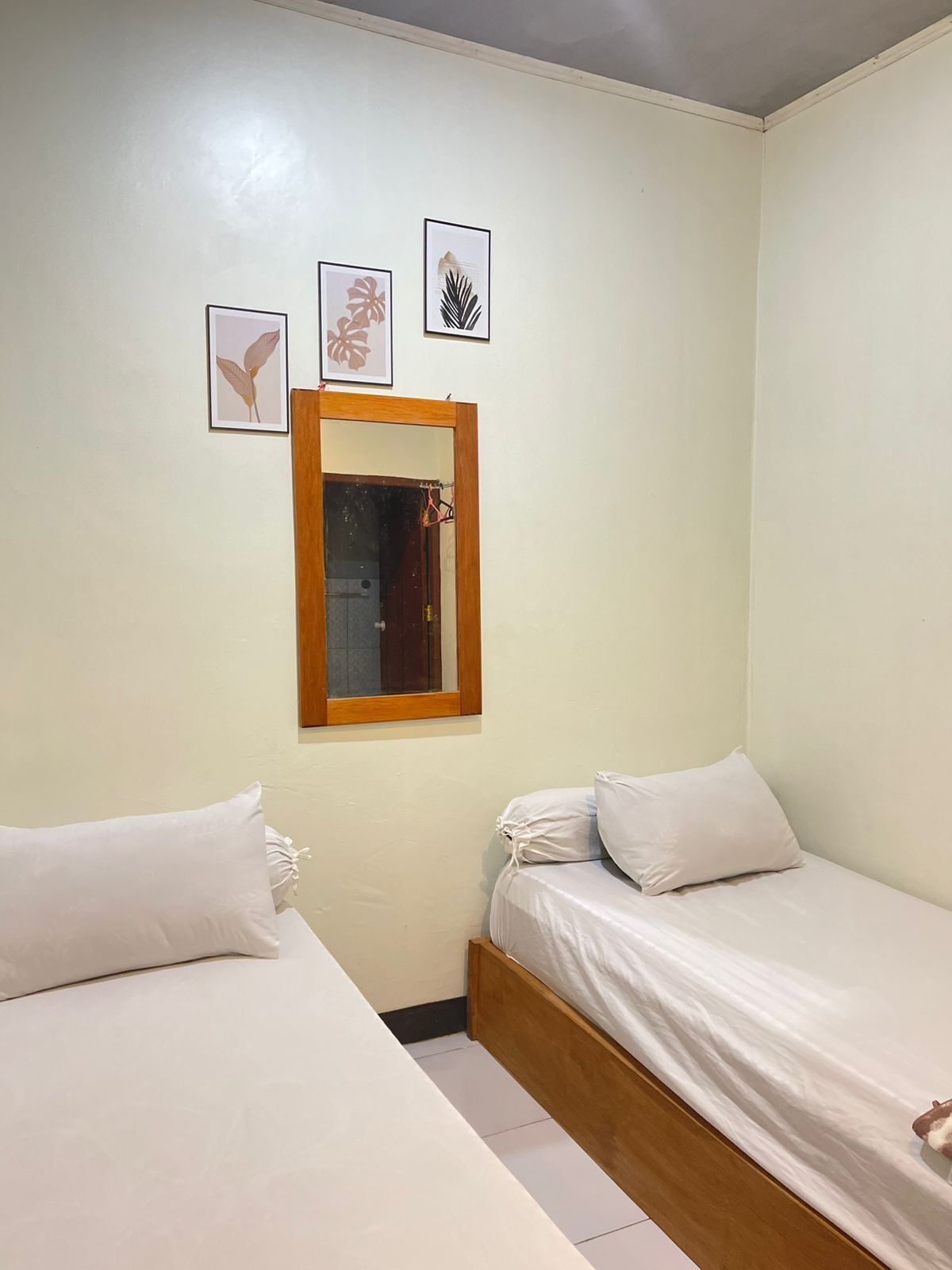 A small, clean room with two single beds, a wooden headboard, and a mirror on the wall.