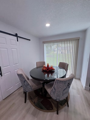 A dining area with a round table, four chairs, a flower centerpiece, and a window with blinds. - Cozy 3BR, 2 BAT Near the World Equestrian Center. (Ocala)