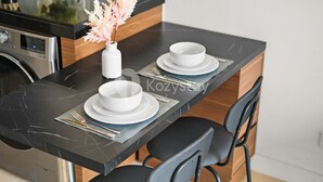 Una cocina moderna con encimera de mármol negro, dos cuencos blancos sobre un plato a juego, un florero con flores secas y un horno empotrado.