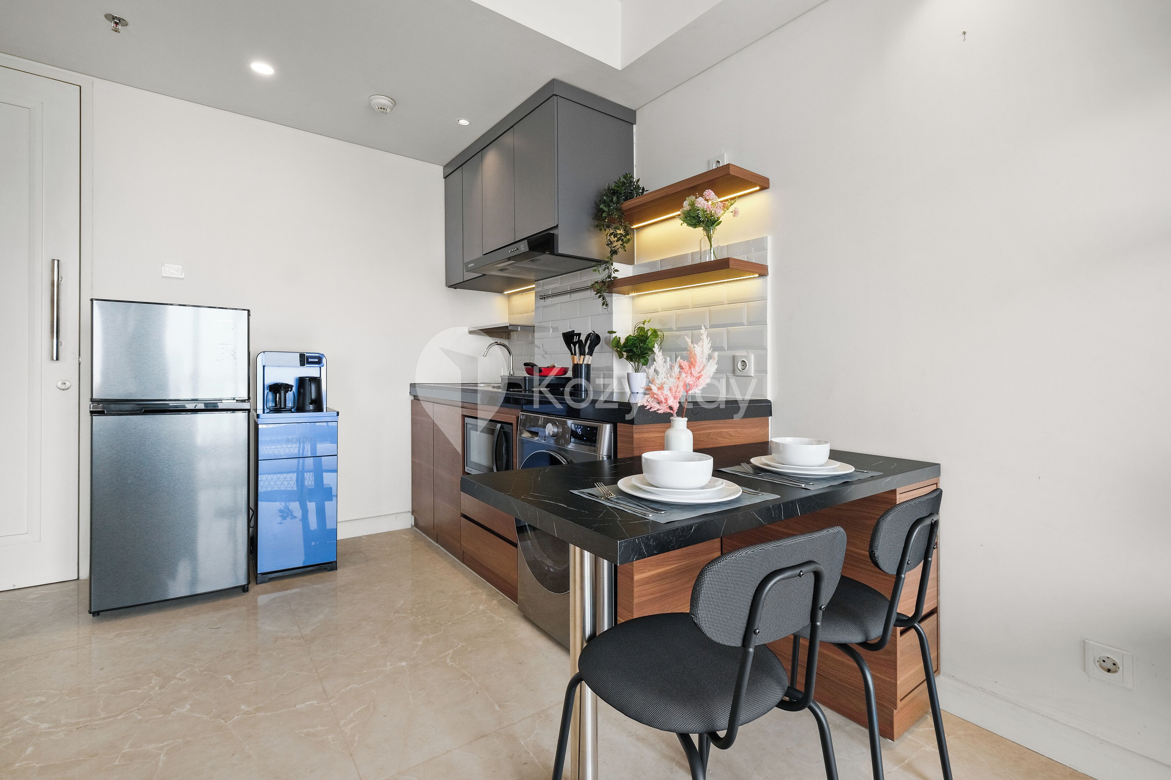 Una cocina moderna con horno integrado, cafetera y comedor con encimera negra y dos sillas.