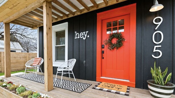 A house with a black exterior, a red door, and the number 9055.