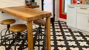 A dining area with a wooden table and stools, a red accent wall, and a black and white patterned floor.