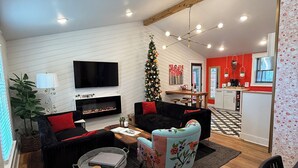 A modern living room with a fireplace, a TV, a Christmas tree, and a dining area with a kitchen in the background.