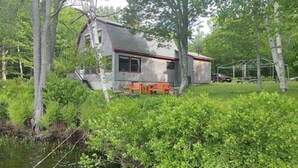 Un chalet rustique avec une façade en pierre, une terrasse en bois et un petit espace extérieur aménagé pour s’asseoir.